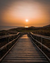 Footbridge over sea against sky during sunset