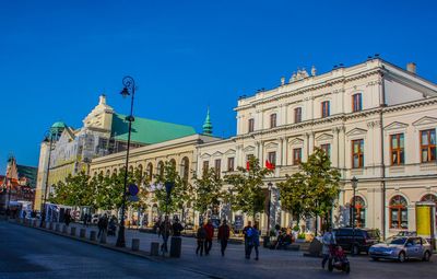 People on street by building against blue sky