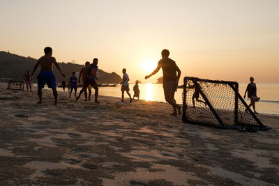 People playing at beach against sky during sunset