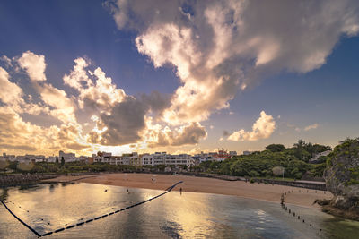 Scenic view of river by buildings against sky during sunset