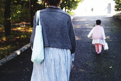 Rear view of mother with daughter walking on road
