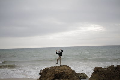 Man jumping at beach against sky