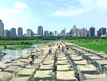 People walking by buildings in city against sky