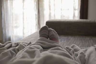 Low section of person wearing socks relaxing on bed at home