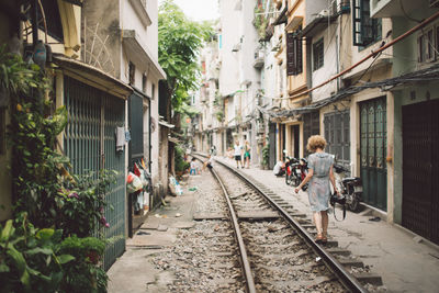 Rear view of woman walking on railroad track amidst buildings in city