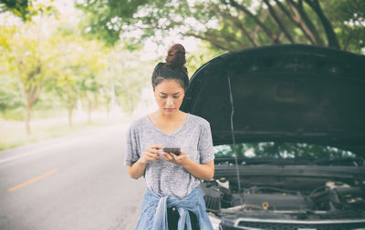 Young woman using mobile phone against breakdown car on road