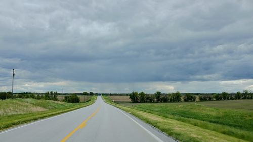 Scenic view of road amidst field against cloudy sky