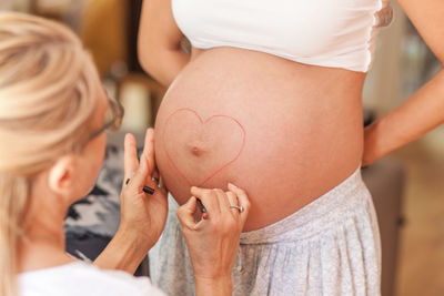 Rear view of woman making heart shape on stomach of pregnant woman