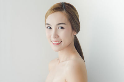 Portrait of smiling topless young woman standing against wall