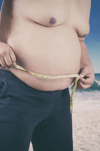 Man measuring abdomen at beach