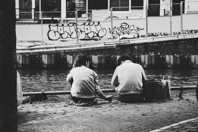 Rear view of men sitting by lake in city