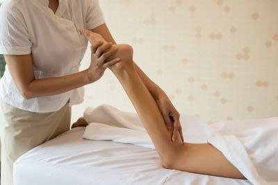 Midsection of masseur massaging leg of woman on table in spa