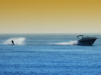 Person waterskiing on sea against sky during sunset