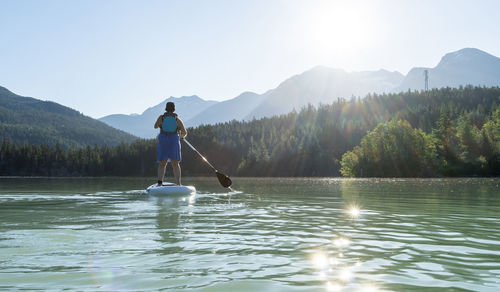 Anonymous female paddleboarding on sunny day on mountain lake
