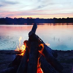 Wooden log on lake against sky during sunset