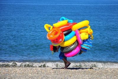 Full length of man carrying inflatable rings while walking shore at beach