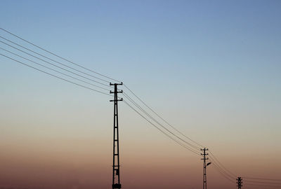 Low angle view of silhouette electricity pylon against clear sky