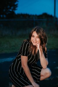 Portrait of cheerful beautiful woman crouching on road at dusk