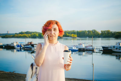 Portrait of mid adult woman talking while standing by river against sky