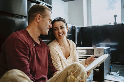 Happy couple discussing over wood in kitchen while renovating home