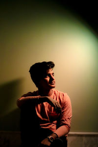 Young man looking away while sitting on wall