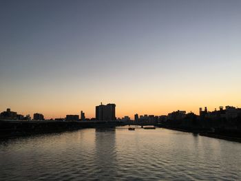 Silhouette buildings by river against sky during sunset