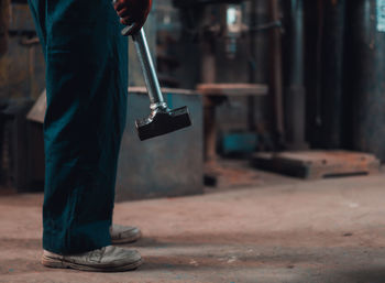 Low section of man holding hammer while standing in factory