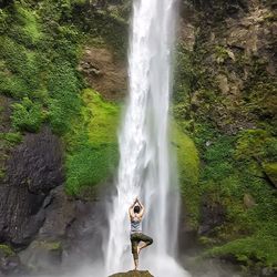 Full length rear view of man performing yoga against waterfall