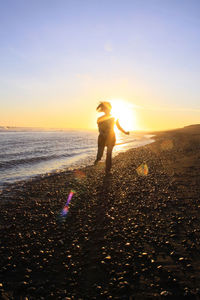 Rear view of woman walking at beach against sky during sunset