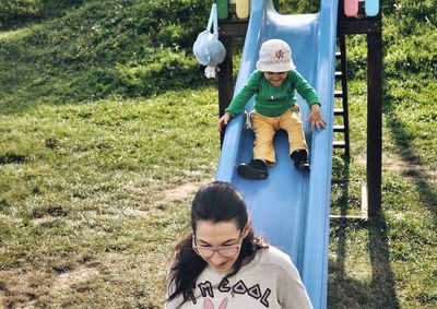 High angle view of mother and son playing on slide at playground