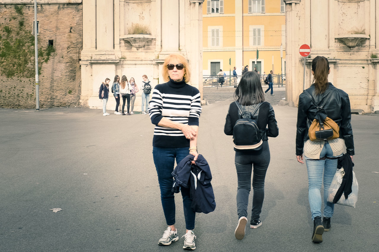 men, lifestyles, person, leisure activity, walking, togetherness, street, building exterior, full length, casual clothing, architecture, large group of people, built structure, rear view, friendship, city, city life, bonding, standing