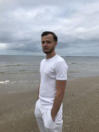 Young man standing at beach against sky