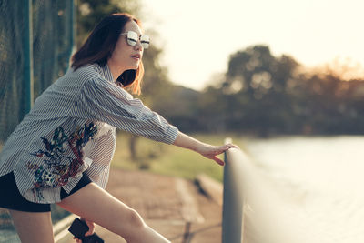 Side view of young woman looking away while standing by railing