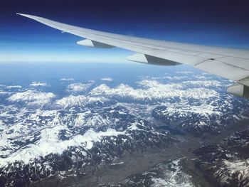 Aerial view of airplane flying over snowcapped landscape against sky