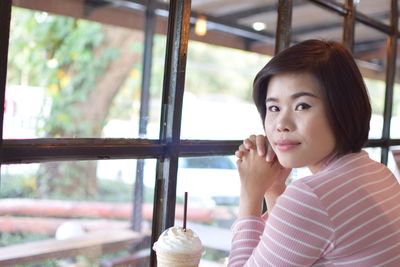 Portrait of young woman sitting with drink on table at cafe