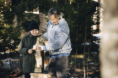 Smiling mature man teaching son to cut log with axe in forest