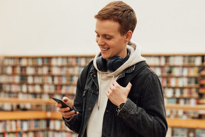 Young man using mobile phone while standing in library