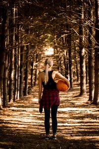 Rear view of woman carrying pumpkin in forest
