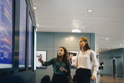 Multi-ethnic female colleagues examining flight timings on arrival departure board at airport