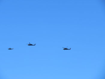 Low angle view of helicopters flying against clear blue sky