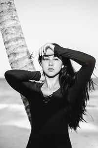 Portrait of young woman standing against tree trunk