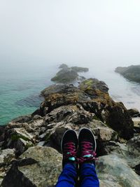 Low section of man standing on cliff by sea against sky