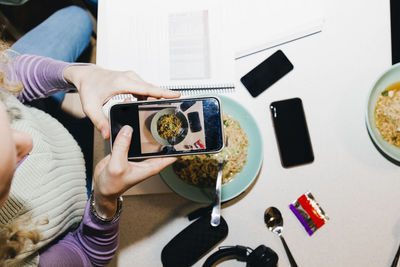 Directly above shot of young woman photographing noodles while studying in college dorm