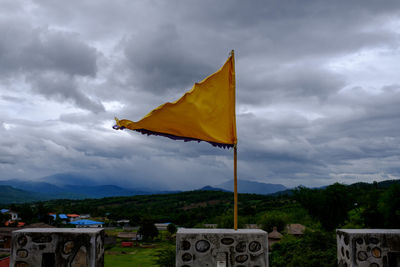 Yellow flag on built structure against cloudy sky
