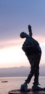 Statue by sea against sky during sunset