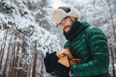 Man holding ice cream standing against trees during winter