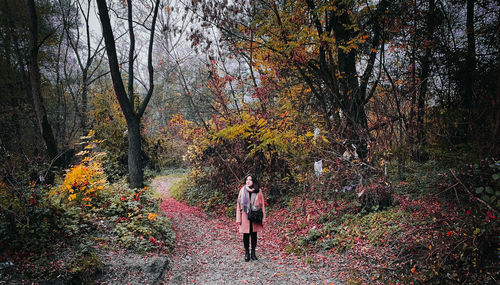 Rear view of woman standing by trees in forest during autumn