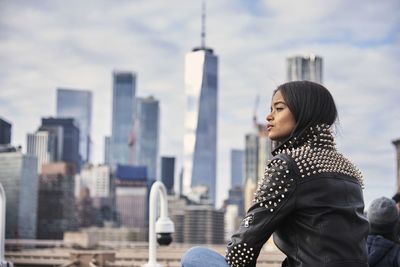 Young woman looking at cityscape against sky