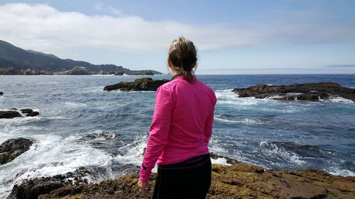 Rear view of woman standing at beach against sky