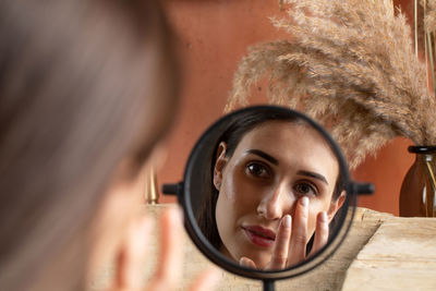 A young woman in front of a mirror applies a moisturizer on her face. beauty portrait